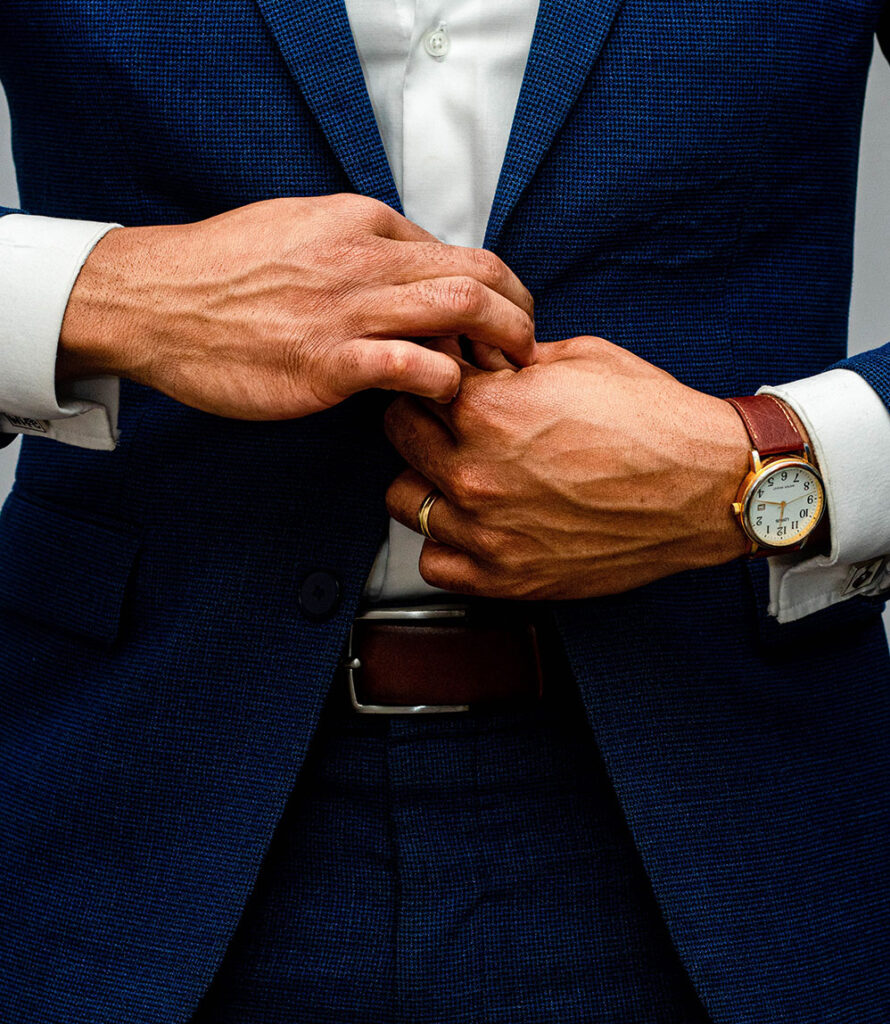 Man in blue suit buttoning jacket, wearing a leather watch and wedding ring